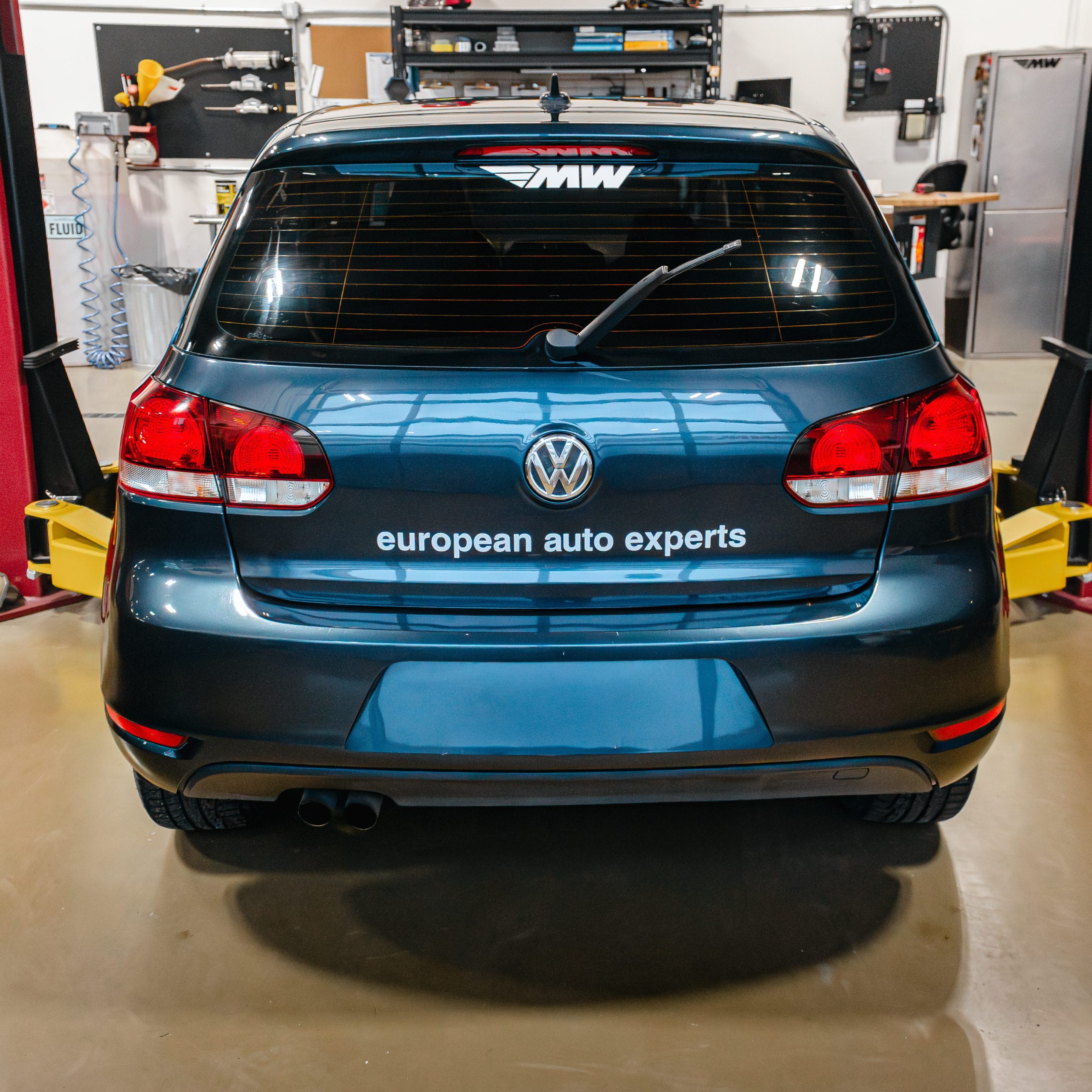 Rear of Volkswagen hatchback in Motor Werke service bay with "European auto Experts" decal - VW repair & maintenance. 